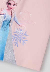 Jasnoróżowa tkanina z grafiką postaci o blond włosach w niebieskiej sukience, ozdobiona brokatem i niebieskim wzorem płatka śniegu.