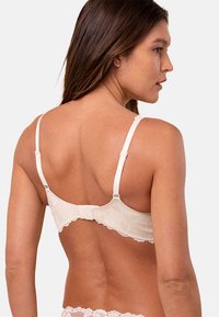 Biszty z koronkowym wykończeniem w jasnym beżowym kolorze, z regulowanymi ramiączkami i zapięciem na haki z tyłu. Gładka tekstura z detalami w kwiatowy wzór.