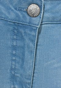 Denim azul claro con una textura suave, que presenta un botón metálico plateado con detalle de marca. Las costuras cosidas son visibles a lo largo del borde.