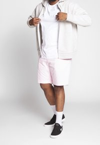 Světle šedá mikina na zip, bílý tričko, růžové šortky, černé tenisky s bílými detaily a bílé ponožky, v uvolněném střihu.