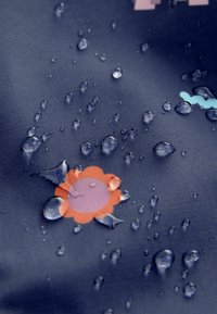 Vodoodporna tkanina v temno modri barvi, ki vsebuje barvite vzorce cvetlic in valov. Površina prikazuje kapljice vode, kar poudarja njene zaščitne lastnosti.