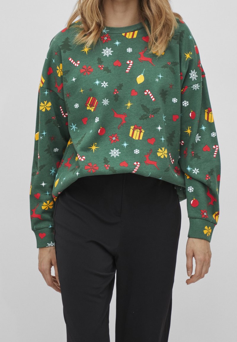 Grön sweatshirt i mjukt tyg, med ett festligt mönster av röda renar, färgglada julklappar och snöflingor. Lös, kort design.
