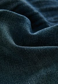 Donkerblauwe denimstof met een zachte, gestructureerde oppervlakte. Subtiele kleurvariaties en fijne weefpatronen zijn zichtbaar.