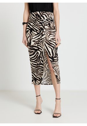 Donna che indossa un top nero e una gonna di media lunghezza con stampa zebrata, spacco frontale e fibbia argento, abbinati a tacchi neri con cinturino alla caviglia.