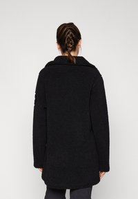 Cappotto nero simile alla pelliccia con un ampio colletto e maniche lunghe, caratterizzato da una vestibilità rilassata e una superficie texturizzata. Nessuna chiusura visibile.