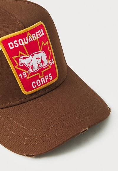 Căciulă maro cu o vizor curbat, dotată cu o patch brodat roșu care reprezintă un urs, accente galbene și textul "DSQUARED2 CORPS 1964."