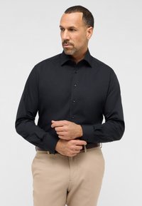 Schwarzes Langarmshirt mit klassischem Kragen, knopfbarem Vorderteil und tailliertem Schnitt. Mit maßgeschneiderten Manschetten und glatter Stofftextur.