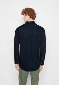 Navyblauwe blouse met lange mouwen, hoge kraag, geknoopte manchetten en een plooi-detaillering aan de achterkant. Gemaakt van een gladde stof.