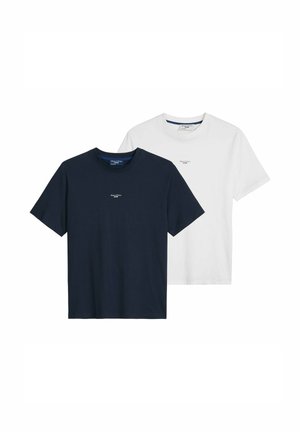 Uomo che indossa una T-shirt bianca Marc O’Polo Denim e jeans blu, accessoriata con una collana a catena in argento e un braccialetto.