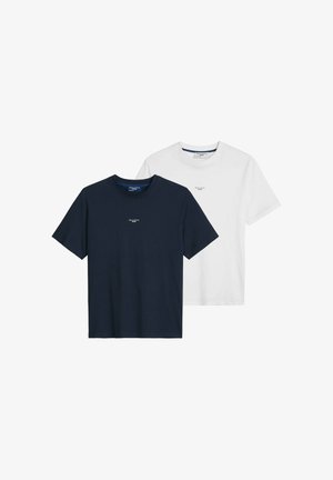 Mann trägt ein weißes Marc O’Polo Denim T-Shirt und blaue Jeans, ergänzt durch eine silberne Halskette und ein Armband.