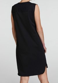 Zwarte mouwloze jurk van zacht materiaal, met een hoge halslijn, zijsplitten en een strakke, eenvoudige ontwerp zonder extra details.