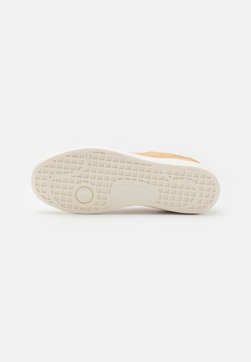La suela de las zapatillas Lacoste presenta una base de goma blanca texturizada con un patrón enrejado y un acento circular, complementada por una sección superior de color marrón.