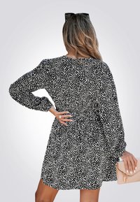 Zwart-wit gestippende jurk met lange mouwen, een getailleerde taille en een uitlopende rok. Glad materiaal met een subtiele glans, gecombineerd met een beige clutch.
