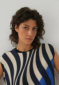 Bedruckte Bluse mit gewellten Streifen in Marineblau, Creme und Hellblau. Hergestellt aus einem glatten, leichten Stoff mit rundem Ausschnitt.