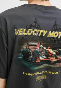 Sort T-shirt med et grafisk billede af en rød racerbils med teksten "VELOCITY MOTOR" og "SONIC PACE CIRCUIT" i gul, slidt skrift.