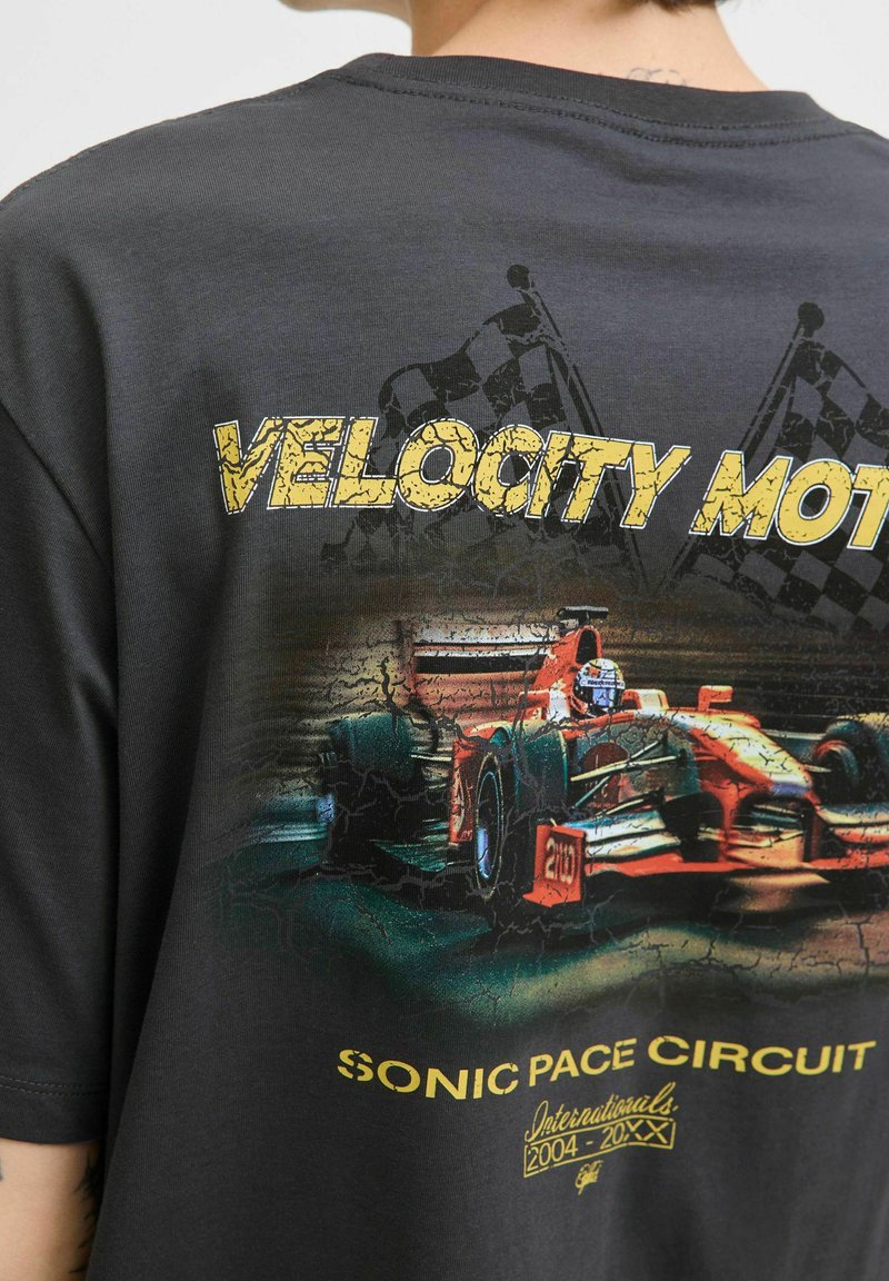 Sort T-shirt med et grafisk billede af en rød racerbils med teksten "VELOCITY MOTOR" og "SONIC PACE CIRCUIT" i gul, slidt skrift.