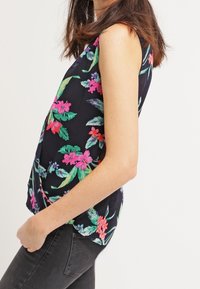 Top de estampado floral con diseño sin mangas, que presenta flores vibrantes en tonos rosa y verde sobre un fondo oscuro de color marino, tejido suave y corte holgado.