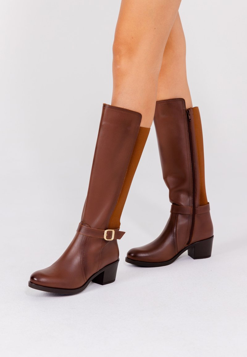 Botas de cuero marrón hasta la rodilla con un panel lateral de color beige, detalle de hebilla y tacón ancho. Equipadas con cremallera interior para un fácil calzado. Textura suave.