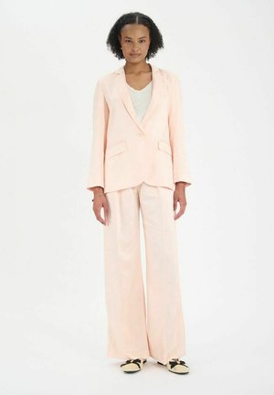 Blazer rose clair à un bouton, associé à un pantalon évasé. Texture de tissu douce, avec des poches plaquées et des manches longues.