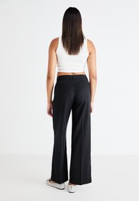 Black pinstripe wide-leg trousers with a smooth texture and back pockets, paired with a white cropped tank top and silver shoes.