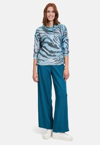 Blå och grå randig pullover med en halsringning, i kombination med lösa turkosa byxor och vita sneakers. Lätt och strukturerad tyg.