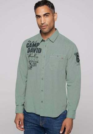 Lichtgroen knoopshirt met een borstzak, voorzien van zwarte grafische tekst aan de linkerkant en een gladde, licht gestructureerde stof.
