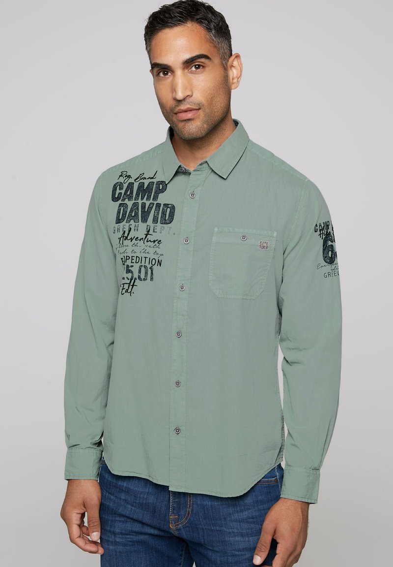 Lichtgroen knoopshirt met een borstzak, voorzien van zwarte grafische tekst aan de linkerkant en een gladde, licht gestructureerde stof.