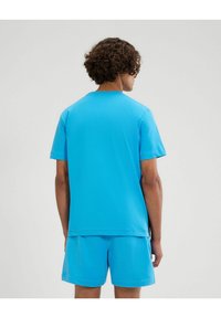 T-shirt in cotone blu chiaro a maniche corte con collo a giro, dotato di una vestibilità comoda e pantaloni coordinati, mostrato dalla parte posteriore.