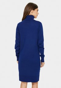Vestito in maglia di un blu profondo con collo alto, maniche lunghe e polsini e orlo ribattuti. Tessuto liscio, silhouette a metà gamba.