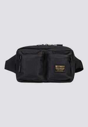 Sac banane noir avec deux poches avant zippées et un patch de marque sur la poche droite, sur fond gris clair.