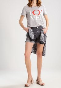 Harmaa T-paita, jossa "LOVE" painettuna punaisella ja valkoisella, yhdistetty mustiin farkkushortseihin. Asusteina mustavalkoinen kuviollinen huivi ja beiget korkokengät.