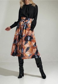 Černý dlouhý rukáv top spojený s rozšířenou midi sukní s geometrickým vzorem v teplých tónech. Černé kozačky nad kolena dotvářejí celý outfit.