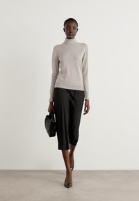 Lys grå turtleneck sweater parret med sorte cropped bukser, sorte spidse hæle og en lille sort taske, mod en neutral baggrund.