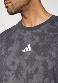 T-shirt gris tie-dye à manches courtes, col rond, tissu texturé et logo blanc Adidas sur le haut à gauche de la poitrine.