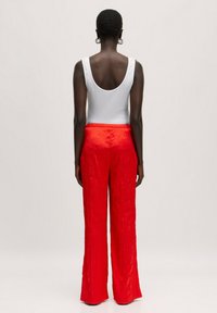 Rode geplooide broek met een wijd gesneden ontwerp, gemaakt van een textuur stof en voorzien van een elastische tailleband, gecombineerd met een witte mouwloze top.