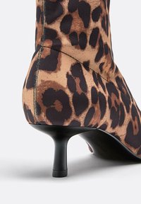 Bottine à imprimé léopard avec une tige en tissu extensible, un bout pointu et un talon haut noir élancé. Coutures visibles sur le côté.