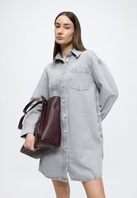 Grå denim skjortekjole med knaplukning og lomme, kombineret med en tekstureret bordeaux læder tote taske med lange, bundne stropper.