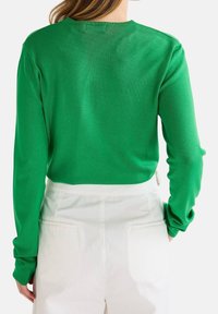 Pull vert en maille avec un col rond et des manches longues, associé à un pantalon blanc taille haute avec des poches arrière.