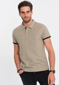 Béžové polo tričko s černým límečkem a akcenty na rukávech. Obsahuje tři knoflíky, krátké rukávy a přiléhavý design.