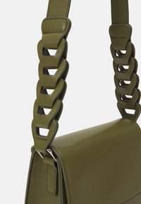 Oliwkowa skórzana torba na ramię z szerokim paskiem, ozdobiona przeskalowanymi ogniwami łańcucha w dopasowanej oliwkowej zieleni.