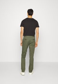 Svart t-shirt med kort ärm, kombinerad med olivgröna chinos. Chinosen har rak passform och två bakfickor. Skorna är vita sneakers.