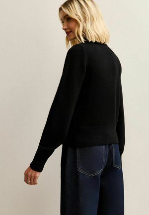 Zwarte gebreide trui met een gestructureerde afwerking, voorzien van lange mouwen en een geribbelde zoom, in combinatie met donkerblauwe spijkerbroeken.