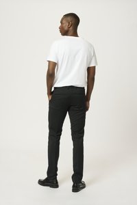 Pantalons noirs ajustés avec une coupe slim, dotés de poches arrière et d'une texture de tissu lisse, associés à un t-shirt blanc uni et des chaussures noires.