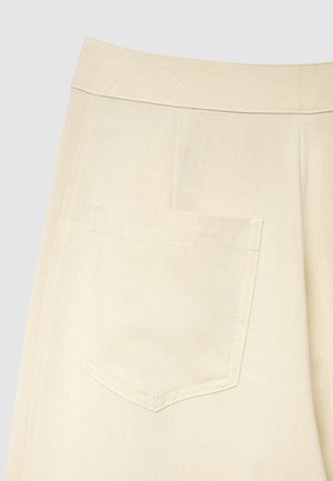Pantalon en lin beige à la texture lisse, doté d'une poche arrière unique avec un haut arrondi et un détail de couture subtil.