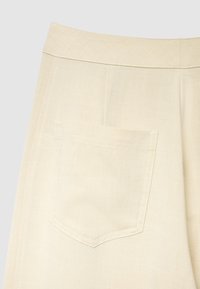 Pantaloni in lino beige dalla trama liscia, caratterizzati da una tasca posteriore singola con bordo superiore arrotondato e una sottile cucitura decorativa.