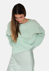 Mintgrüner gerippter Pullover mit weitem Halsausschnitt und langen Ärmeln, kombiniert mit einem leichten Satinrock. Strukturierter Stoff mit lockerer Passform.