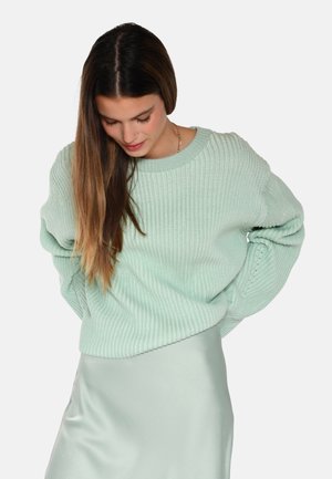 Maglione a coste verde menta con scollatura ampia e maniche lunghe, abbinato a una gonna leggera di satin. Tessuto testurizzato e vestibilità ampia.