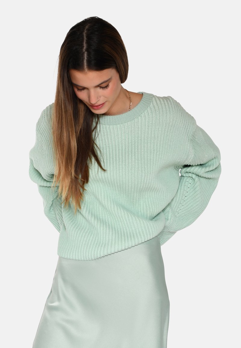 Mintgrüner gerippter Pullover mit weitem Halsausschnitt und langen Ärmeln, kombiniert mit einem leichten Satinrock. Strukturierter Stoff mit lockerer Passform.