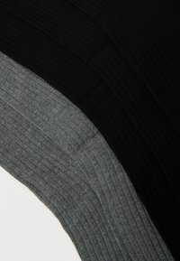 Nærbillede af ribbet stof i sort og mørkegrå farver, der viser strikket tekstur og buede overlappende kanter.