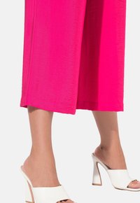 Fuchsia wijde culottes gemaakt van lichtgewicht stof, gecombineerd met witte open-toe block-hak muilen met een ronde band.